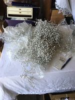Large bundles of small white pearl-like beads clustered together, placed on white cloth with packaging and pen for scale