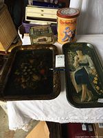 Photo showing four vintage trays and tins on a table including a Cracker Jack tin, Coca-Cola tray, toile tray, and green vintage tin.