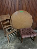 Lot with wooden chair missing its cane seat, round wood table top with distinct patterned grain, and dusty rose upholstered ottoman.