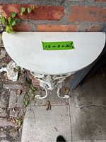 Top view of white metal half moon table with size label 15 x 7 x 32 1/2 inches.