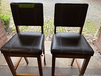 Two dark brown bar height chairs with padded seats and backs shown from front view.