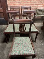 Five solid oak dining chairs with carved harp scroll backs and patterned green upholstery, arranged in garage setting against brick wall.
