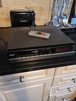 Full view of RCA Beta VCR with remote control on top, placed on kitchen counter.