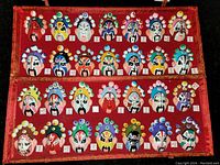 Full view of all 24 hand painted vintage face masks arranged in the red velvet-lined presentation case showing their variety and detailed designs.