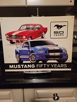Full view of metal sign showing both classic and modern Mustang cars and 50 Years logo