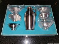 Top view of the sake set showing the bottle in the center and six cups, four cups on right side stacked in pairs and two cups on left side, all in blue foam holder inside presentation case.