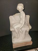 Front angle of the white marble female sculpture showing the figure's pose on chair and walnut base.