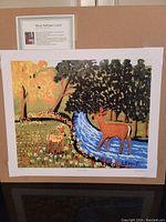 Full view of the unframed lithograph mounted on backing, showing the artwork titled 'Deer At Stream' by Maud Lewis.
