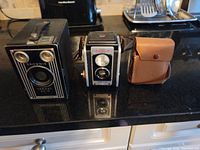 Brownie Target Six-16 box camera, small black box camera, and leather transistor radio visible on black countertop.