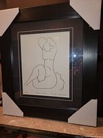 Framed fine art print by Henri Matisse titled Femme Nue, showing line drawing of nude figure in seated pose, in dark brown wooden frame with protective corners.