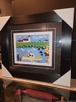 Photo showing the framed artwork from an angle highlighting the matte black wood frame and protective corners.