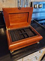 Wooden music jewelry box opened to show velvet-lined compartments and removable tray with ring slots.