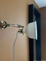 Photo showing close-up of one IKEA wall lamp mounted on beige wall, featuring black articulated arm, white conical shade, and spring mechanism on arm.