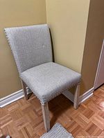 Full view of a single used accent chair with light gray fabric upholstery and metal nailhead trim on edges. Features wooden legs with a natural finish.