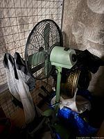 Front side view of the vintage green metal standing fan showing blades, grille, and standing base