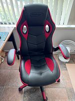 Front view of a used VitaLogic gaming chair showing padded seat and contoured backrest in black and red upholstery with armrests and caster wheels.