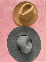 Two wide-brimmed felt hats, one camel color, one grey, placed flat on pink surface