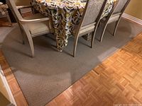 Beige carpet rug under a dining table with six chairs, showing carpet pattern and condition.