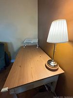 Desk surface with a metal lamp and raised white stand. The desk is wooden and repainted, showing natural wood grain and two small holes on surface.