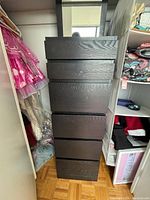 Full view of the tall dark wood drawer chest standing vertically between closet shelving, showing six drawer fronts with wood grain texture.