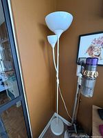 Full view of the white IKEA floor lamp positioned in a corner showing the two bulb fixtures and round base.