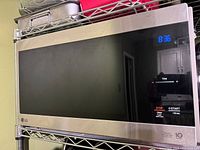 Front view of LG stainless steel microwave oven with digital clock showing 8:36 and control dial on the right side.