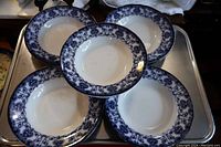 Five of the flow blue bowls arranged with one centered on top showing the blue patterned border and white center.