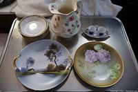 Set of 11 pottery pieces including bowls, plates, jug, tray and cups arranged on metal table.