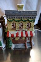Detailed front view of the Coffee Shop Christmas village house with tan brick facade, red and white awning, and greenery decor