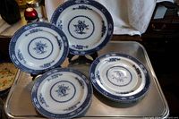 Six flow blue plates displayed on a metal tray, showing a mix of 9-inch and 10-inch plates with blue floral and vase design.