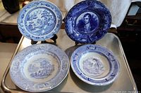 Front view of four antique blue and white plates and bowls showing traditional patterns including flow blue and Willow designs.