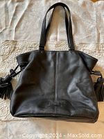 Front view of black Cole Haan leather purse showing pebbled texture and tassels on the sides.