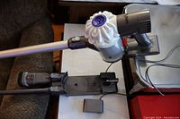 Dyson stick vacuum attached to wand, dock, and accessories laid out