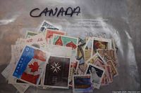 Plastic bag labeled 'Canada' filled with medium-sized used stamps featuring Canadian themes such as the Canadian flag with maple leaf and historic commemorations.
