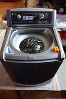 Front top view of LG mini washing machine showing open drum and control panel with settings and dial, missing lid, orange block on right edge.