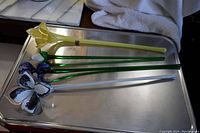 Four Murano glass flowers displayed on a metal tray; three blue, one yellow, each with long green stems.