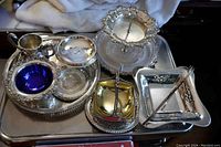 Full view of all 11 pieces in lot arranged on a tray showing variety of silver plated serving ware including a two-tier stand, trays, dishes and bowls.