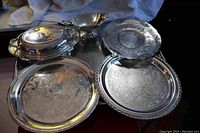 Six-piece silverplate lot showing four round trays, one oval covered serving dish, and one gravy boat arranged together