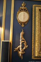 Resin wall plaque with classical bas-relief figure above matching scroll candle sconce on blue wall