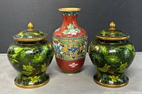 Front view of set showing two green cloisonné pots with lids and one red cloisonné vase.