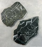 Two soapstone plaques with white etched animal images shown together on light fabric background.
