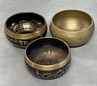 Three singing bowls arranged together showing black and gold colors with intricate engraved designs and scripts.