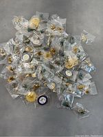 Multiple pins individually bagged with a mixture of gold-toned and enamel colors on gray surface.