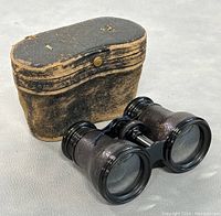 Binoculars next to closed leather case showing worn leather exterior.
