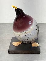 Front view of glossy art glass penguin figurine on black base showing purple upper body fading to white lower body with painted trees and birds.