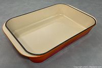 Front angle view of the rectangular Le Creuset cast iron casserole pan showing orange exterior and cream interior with black rim.