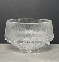 Side view of clear textured glass serving bowl showing tall cylindrical shape with textured vertical lines on upper half and rough, droplet-like glass footed base.