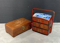Two vintage boxes displayed side by side showing size and design contrast, jewelry box with carved lid and Chinese red lacquer tiered lunch box with blue-white ceramic top.