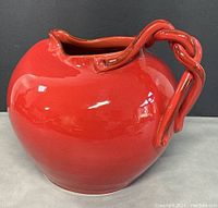 Side view of the bright red ceramic pitcher jug showing the bulbous shape and twisted handle.