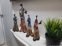 Four jazz musician figurine statues displayed on a white surface with a plant in the background. Showing overall group and scale.